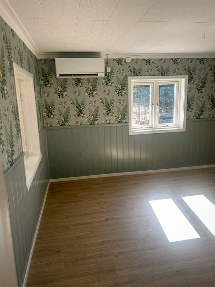 Rum med tapet med ormbunkar och vita blommor ovanför en gröngrå panel