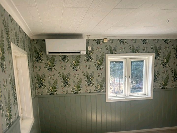 Rum med tapet med ormbunkar och vita blommor ovanför en gröngrå panel